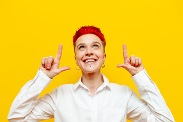 young short-haired red-haired girl points with her hands up on a yellow isolated background,...