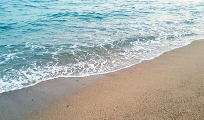 Clear transparent sea water and waves in sunny day with much sand and stones.