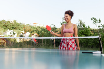 young african american girl playing table tennis outdoors in the park, woman hitting the ball with...