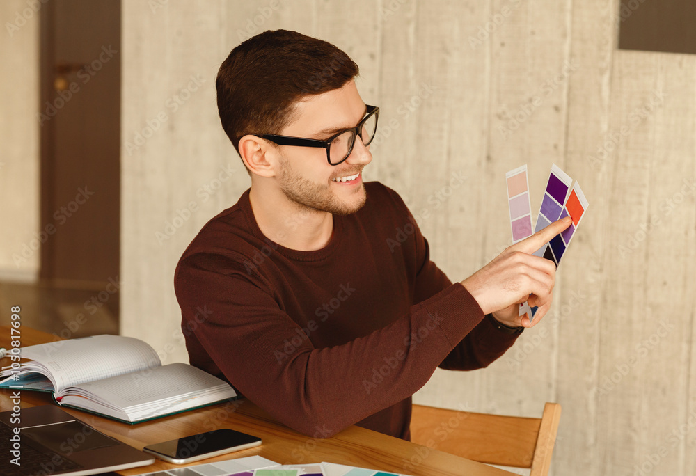Poster designer guy choosing color samples for his project sitting at workplace in modern office. selective