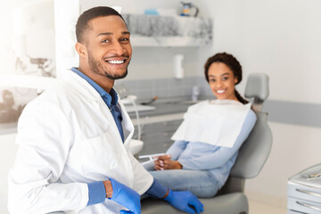 Visiting dentist. Black dentist doctor and female patient in chair smiling at camera, clinic...