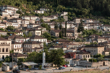 The small city of Berat in Albania with traditional Ottoman-style white stone houses, surrounded by lush greenery. The buildings have brown-tiled roofs, creating a harmonious landscape 