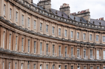 A curved row of tall, elegant buildings with symmetrical windows and balconies. The buildings are made of light-colored stone and have a classic architectural style.