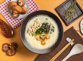 Preserved Egg Chicken Porridge with mushroom,chopsticks and spoon served in bowl isolated on wooden table top view of taiwan food