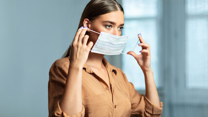 Disease Prevention. Portrait of beautiful girl putting on mask to prevent virus, using laptop, copy...