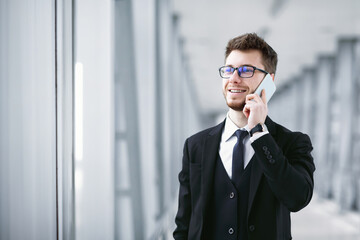 Always In Touch Concept. Handsome entrepreneur talking on phone, wearing eyeglasses, blurred background