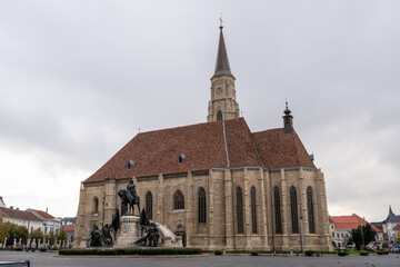 Cluj-Napoca, Romania, October 20, 2024: St. Michael's Church and the Matthias Corvinus Statue in...