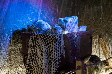Turda, Romania, October 20, 2024: A mining cart filled with salt blocks illuminated by blue and purple lights inside Salina Turda, highlighting the mine's industrial heritage and geological history.