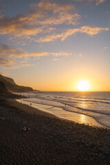 Strandspaziergang bei Sonnenuntergang mit goldenem Himmel und sanften Wellen