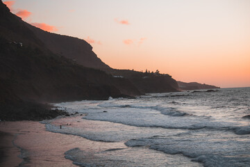 Dramatischer Sonnenuntergang an einer felsigen Küste mit sanften Wellen und farbenfrohen Wolken