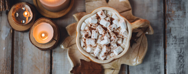 Flat lay top view. Spicy sweet fall hot drink: delicious pumpkin latte with cinnamon, marshmallow. Served in handmade artisan mug in shape of pumpkins, cozy home decor with candles, dry leaves banner