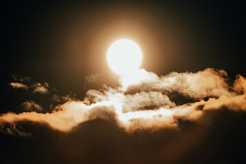 Bright sun illuminating fluffy clouds at dusk over a serene landscape, creating a warm golden glow...