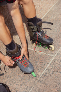 Young man tying laces on inline skates outdoors