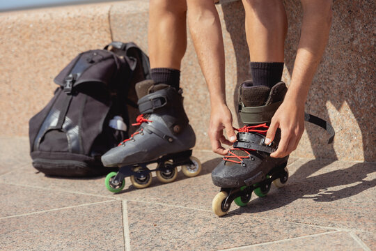 Young man tying laces on inline skates outdoors