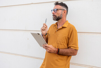 Thoughtful gay man with pride bracelet holding tablet and pen