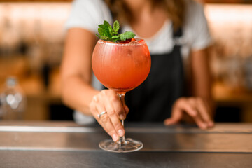 Close-up shot of a tall glass with a cold orange cocktail with mint leaves