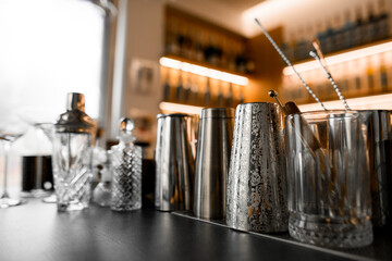 Professional bartender utensils - metal shakers, glasses of different shapes and sizes, long bar spoons stand on the table