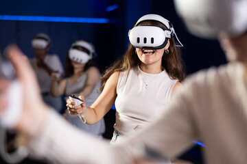 Excited young girl sitting with handheld controllers in hands engaged in virtual world experiencing...