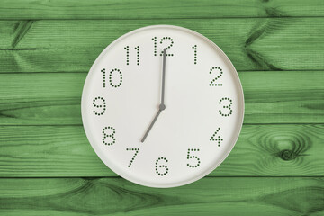 Wall clock shows time 7 o'clock on green wooden background. Round wallclock front view. Nineteen o'clock. brand new day, fresh start, fresh energy, new opportunities