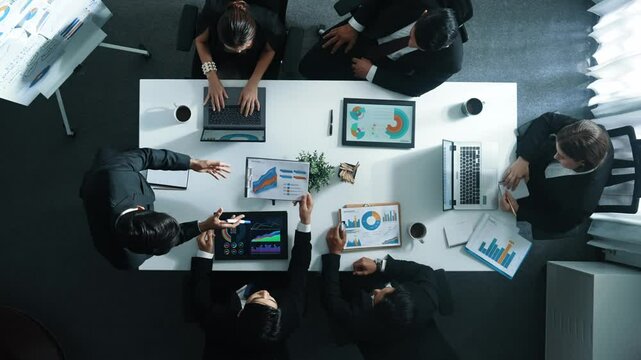 Top down aerial view of manager standing and present marketing plan to skilled investor. Diverse business team working together to analyze financial statistic graph at meeting table. Directorate.