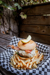 Cheese Burger with bacon and pickle on top over french fries on patio table