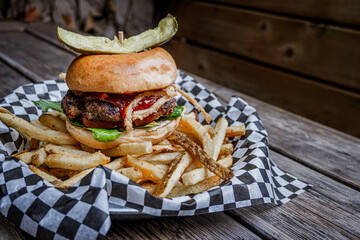 Burger with fried onions and pickle on top over french fries on patio table
