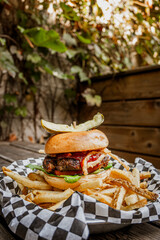 Burger with fried onions and pickle on top over french fries on patio table

