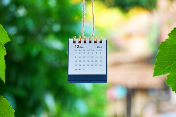 The calendar for December 2024 is hanging with a bokeh garden background. Goodbye 2024. New Year...