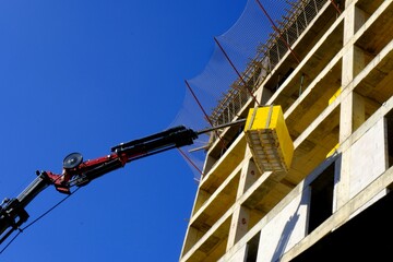 Concrete lifting crane transports concrete blocks to the building under construction. Housing...