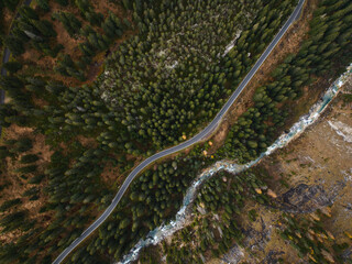 Aerial view of winding Mountain Road and flowing River in a Forest Mountain Landscape in the Swiss Alps during Autumn
