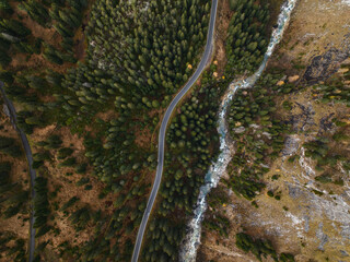 Aerial view of winding Mountain Road and flowing River in a Forest Mountain Landscape in the Swiss Alps during Autumn