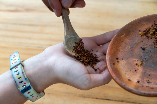 A mixture of cocoa powder and cane sugar being spooned into a child's hand