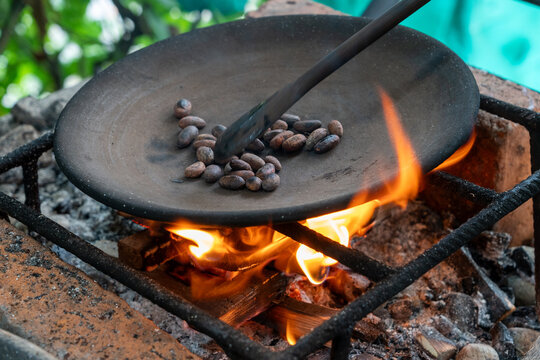 Cacao beans roasting over a fire on a primitive grill. They are being turned with a spoon