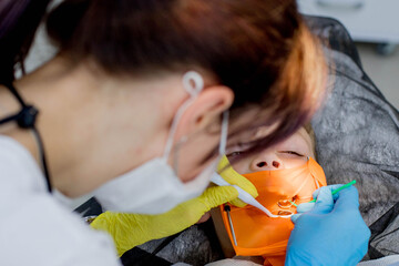 Children's dentistry. First examination at the dentist. A cute handsome boy with his mouth open is looking aside while the doctor is treating her teeth.