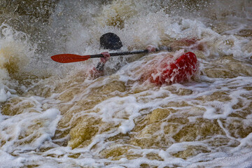 Ein Wildwasser Kajakfahrer versinkt im reissenden Fluss und taucht kurz darauf wieder aus den...