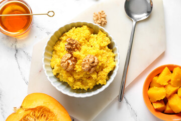 Bowl of tasty millet porridge with pumpkin, honey and nuts on white marble background