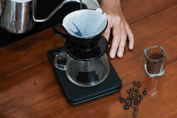 Closeup of a hand pour hot water to wet paper filter on dripper, coffee brewing process v60, making...