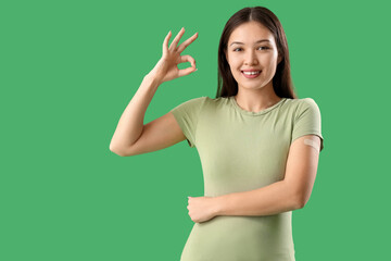 Beautiful young woman with applied medical patch showing OK gesture on green background