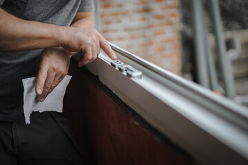 A young man smears the putty in the window frame with his finger.