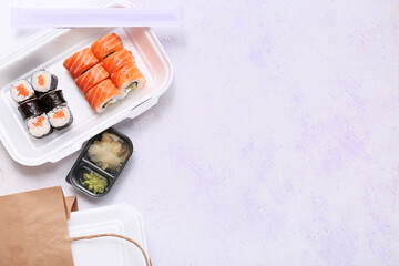 Plastic container with tasty sushi rolls, marinated ginger and paper bag on lilac grunge background. Delivery concept