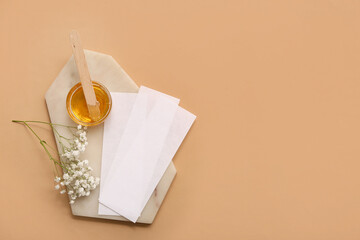 Glass bowl with sugaring paste, wax strips, wooden stick and gypsophila flowers on brown background