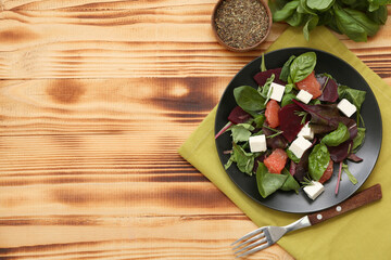Plate with healthy vegetable salad, napkin, bowl of herbs and fork on wooden background