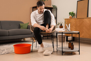 Handsome young happy man with tools cutting cuticle and doing pedicure at home