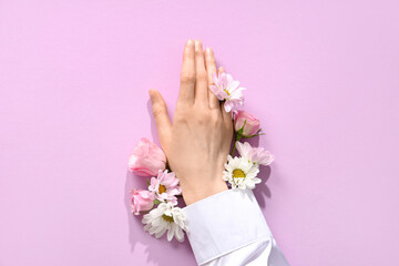 Female hand with different fresh flowers on lilac background. Care concept