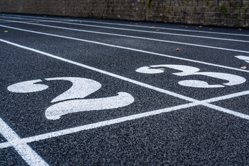 Close up lane number 2 on a new black running track with white lane lines and other markings.	
