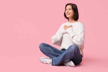 Thankful young woman pressing hands to chest and smiling on pink background