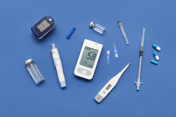 Glucometer with lancet pen, insulin and thermometer on blue background. Diabetes concept