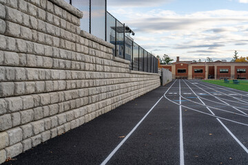 Segmental retaining wall next to a new black running track with white lines.	