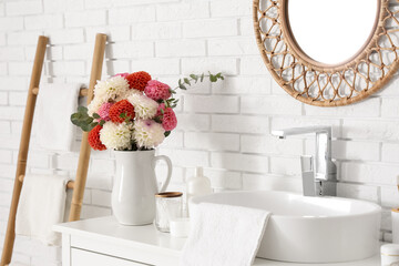 Bouquet of beautiful dahlia flowers and bath supplies near sink in light bathroom