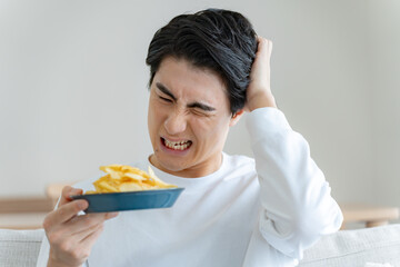 ポテトチップスを持ちながら考える男性